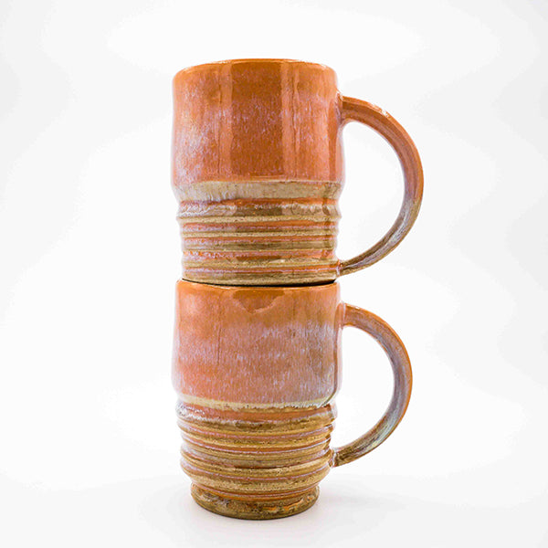 Side photo of stacked pair of  stoneware  mugs with orange glaze handmade by Allison Morrissey